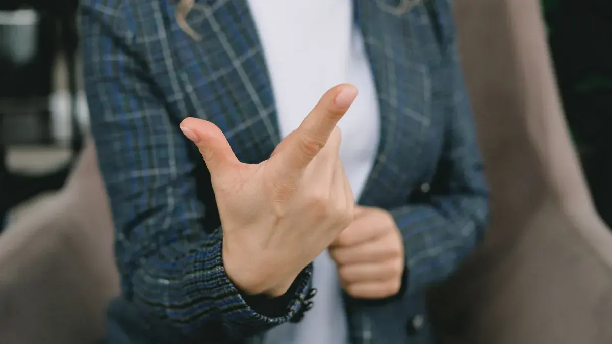 Mulher de blazer com a mão em destaque, ilustrando dor na ponta do dedo indicador