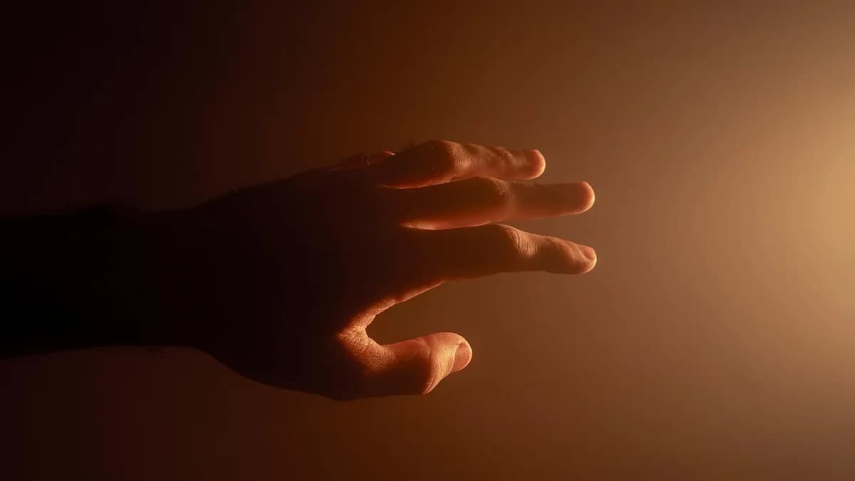 Mão estendida em ambiente escuro sob luz quente, representando queimação nas mãos à noite