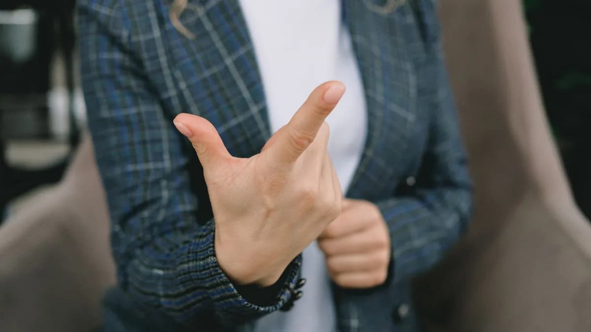 Mulher de blazer com a mão em destaque, ilustrando dor na ponta do dedo indicador